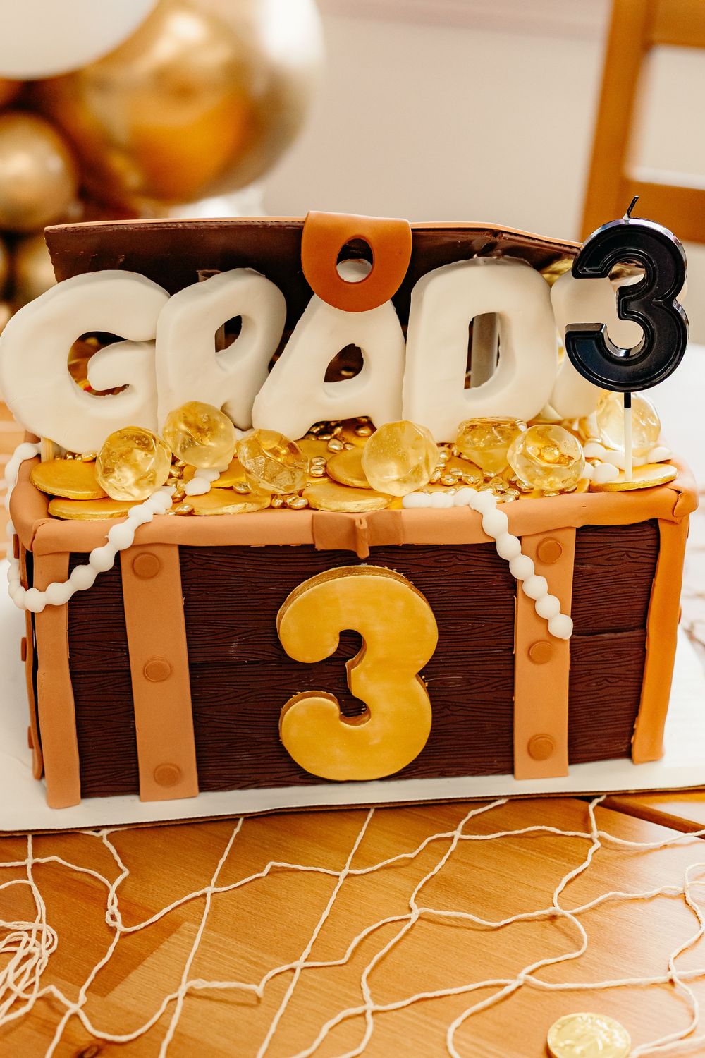 A treasure chest-themed birthday cake decorated with gold coins and numbers 3 showing a pirate party design.