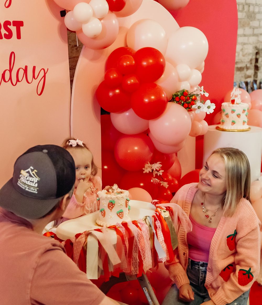 People celebrating at a party with red and white balloon decorations and a gift wrapped in pink paper.