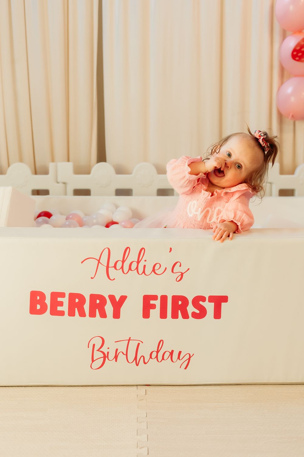 A festive first birthday setup with pink and white decor featuring text 'Berry First Birthday' against a light backdrop.