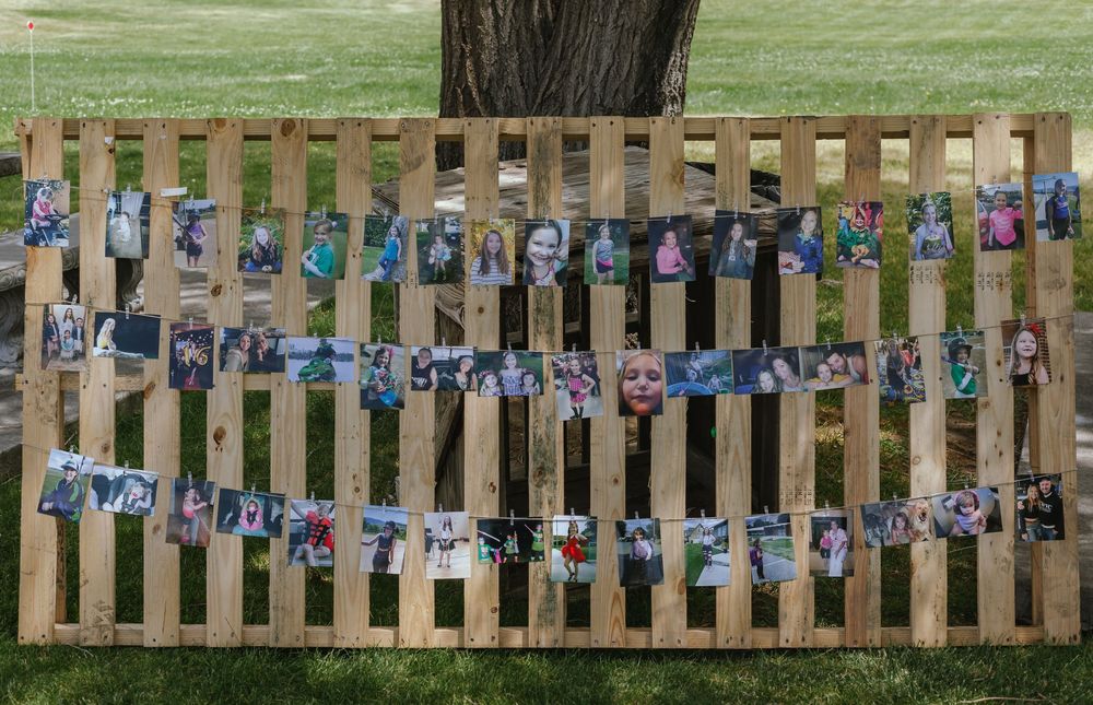 Multiple photographs displayed on string lines against a wooden fence panel in an outdoor setting.