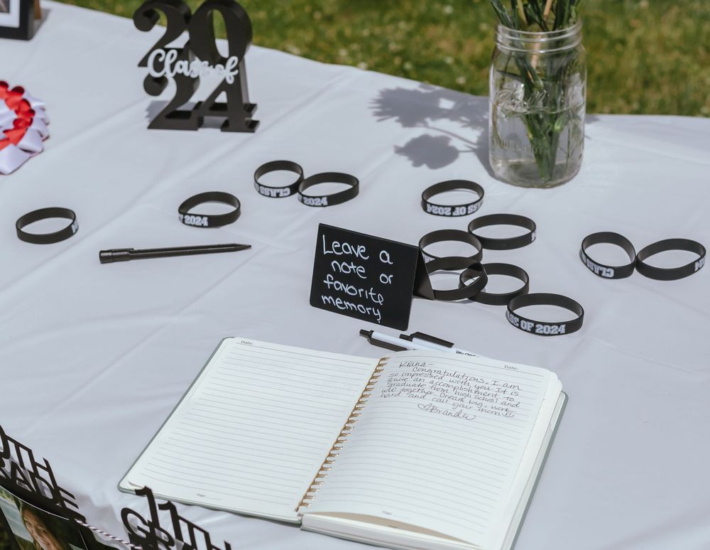 Open guest book with black silicone bracelets displayed on white tablecloth at outdoor event.