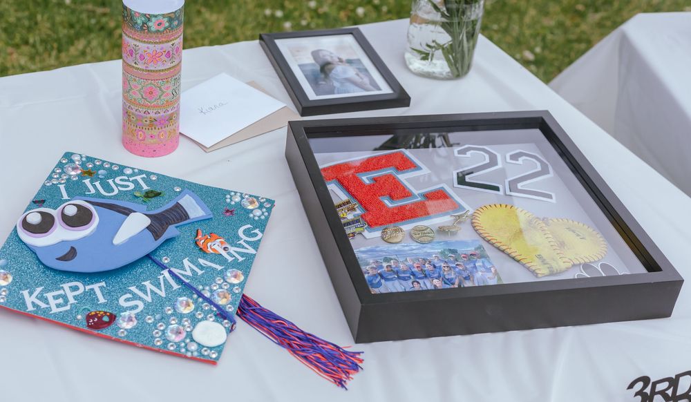 Graduation memory items including decorated frames and keepsakes displayed on a white tablecloth outdoors.