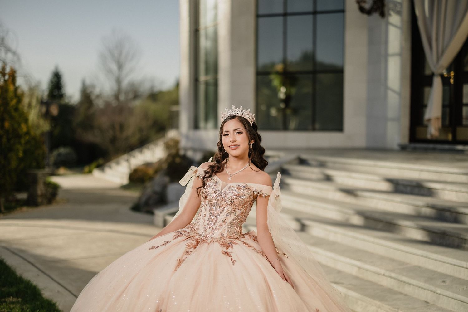 Elegant black ball gown posed on stone steps of classical building.