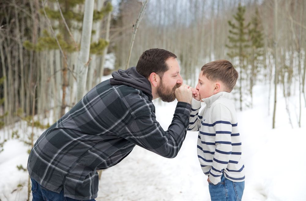 A tender winter moment between parent and child amidst snow-covered trees.