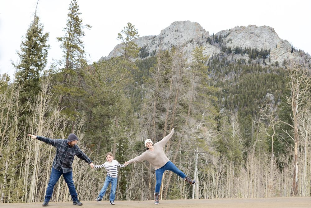 Three people strike playful yoga poses against a backdrop of mountain peaks and aspen trees.