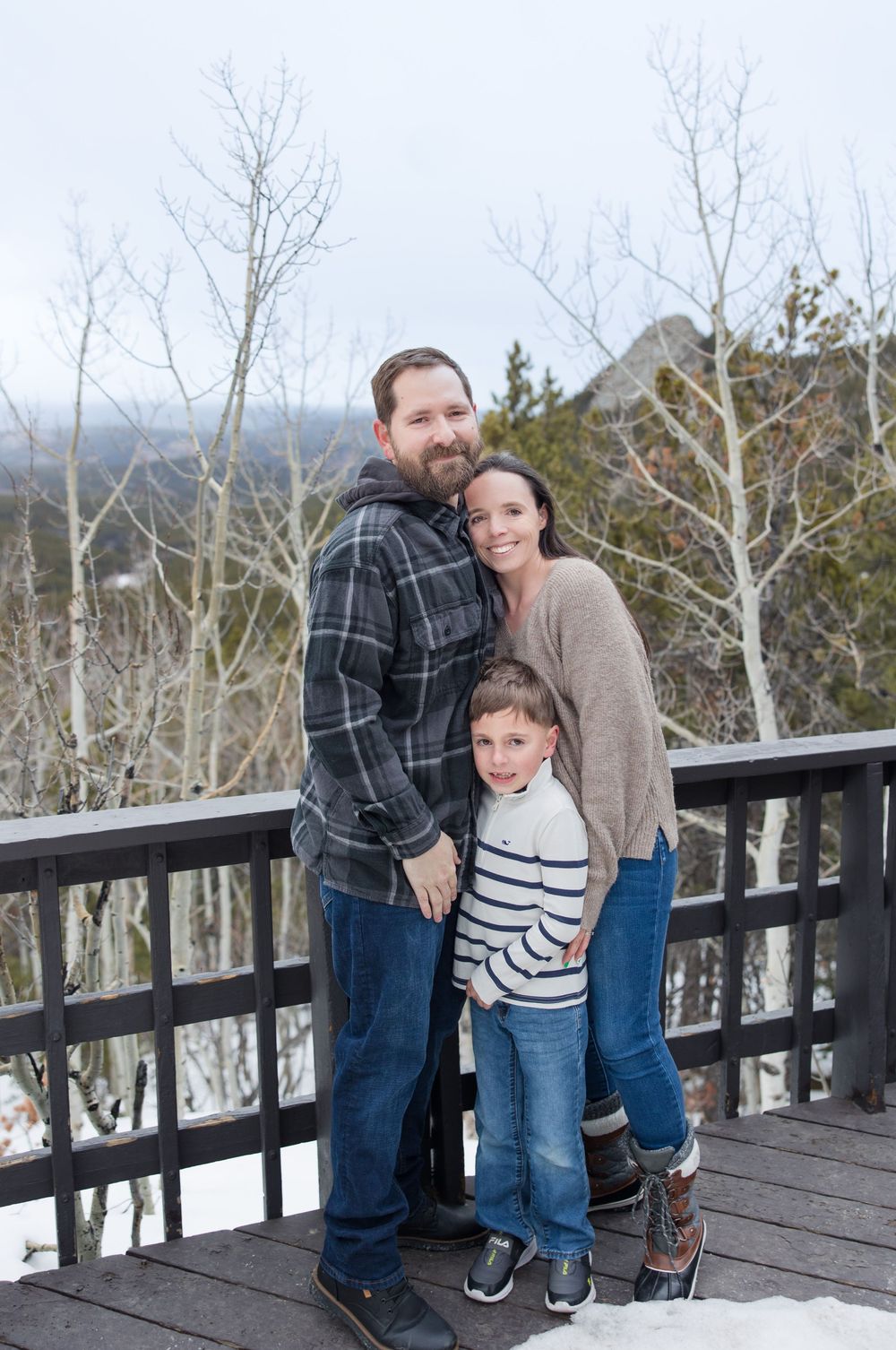 A family stands together on a wooden deck overlooking a snowy mountain landscape.