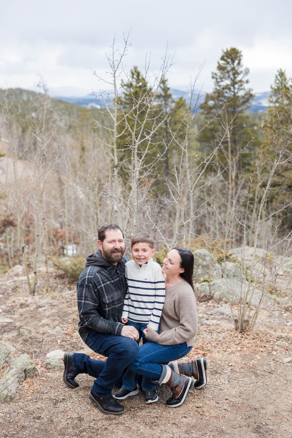 A family poses together on a mountain trail surrounded by bare trees and evergreens in winter.
