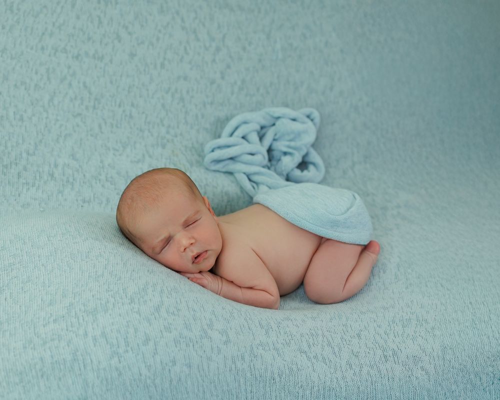 Sleeping newborn baby curled up peacefully on soft mint-colored blanket with tiny angel wings.