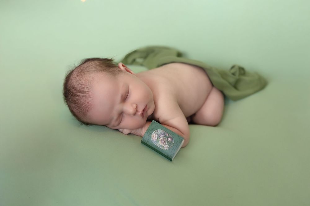 Sleeping newborn baby on mint green background with tiny wallet displayed beside them.