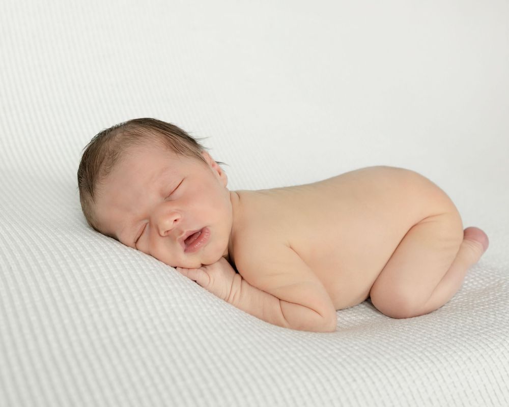 Peaceful newborn baby sleeping on white textured fabric in natural light.