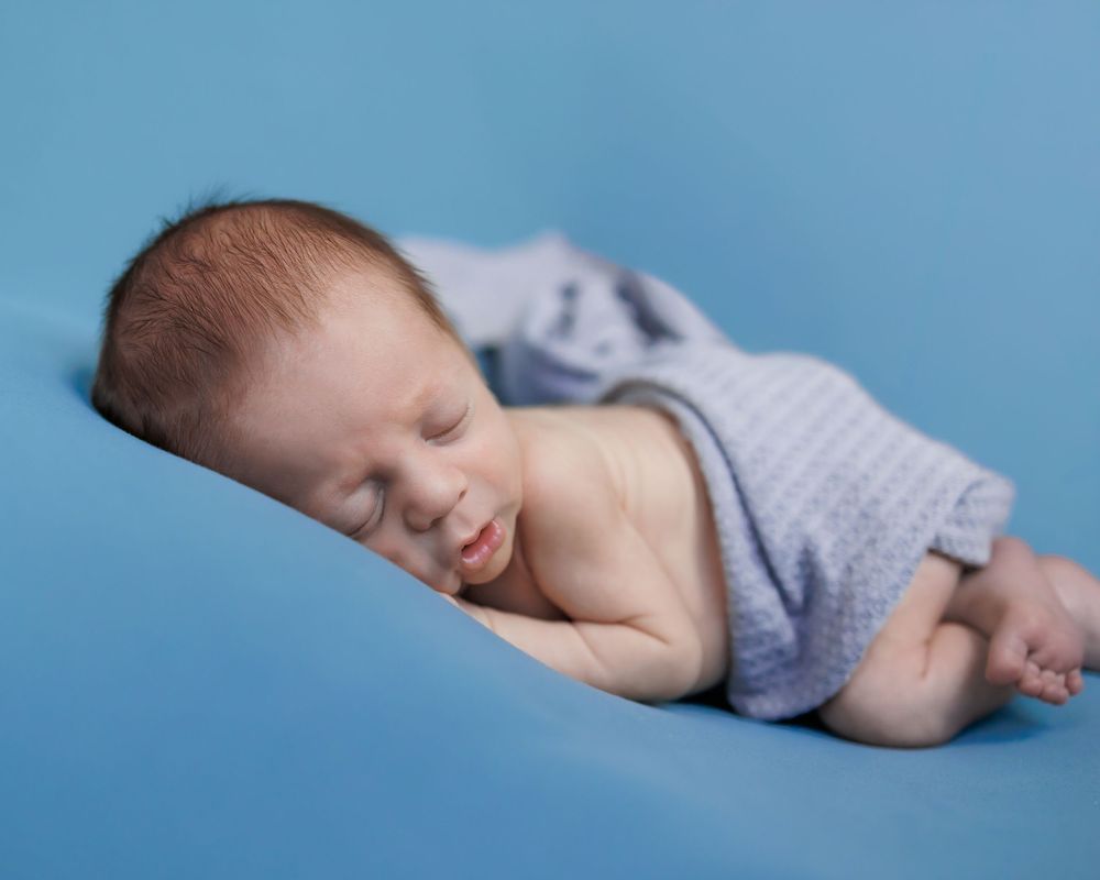 Sleeping newborn baby wearing light blue shorts rests peacefully on blue background during professional photo session.