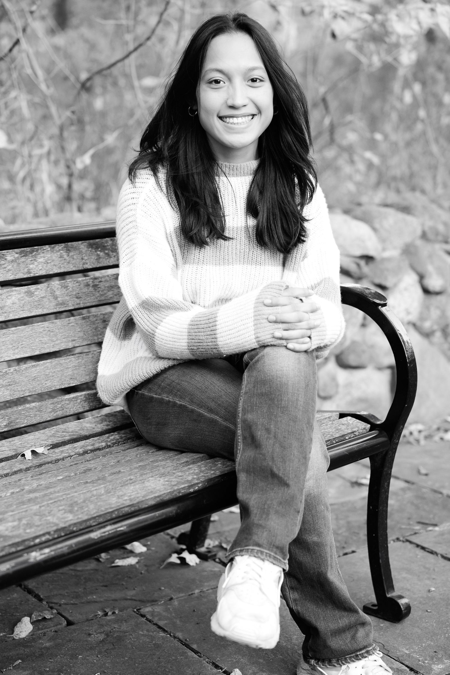 Black and white portrait of someone in a white sweater sitting relaxed on a wooden park bench.