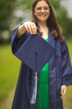 Close up of graduation cap with tassel held by graduate in navy gown.