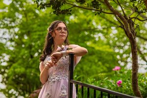 Person in lavender gown poses gracefully on garden balcony.