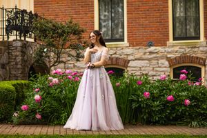 Person in flowing pink formal gown poses in garden with blooming roses.