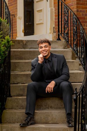 Professional portrait on brick steps wearing black suit with ornate iron railing.