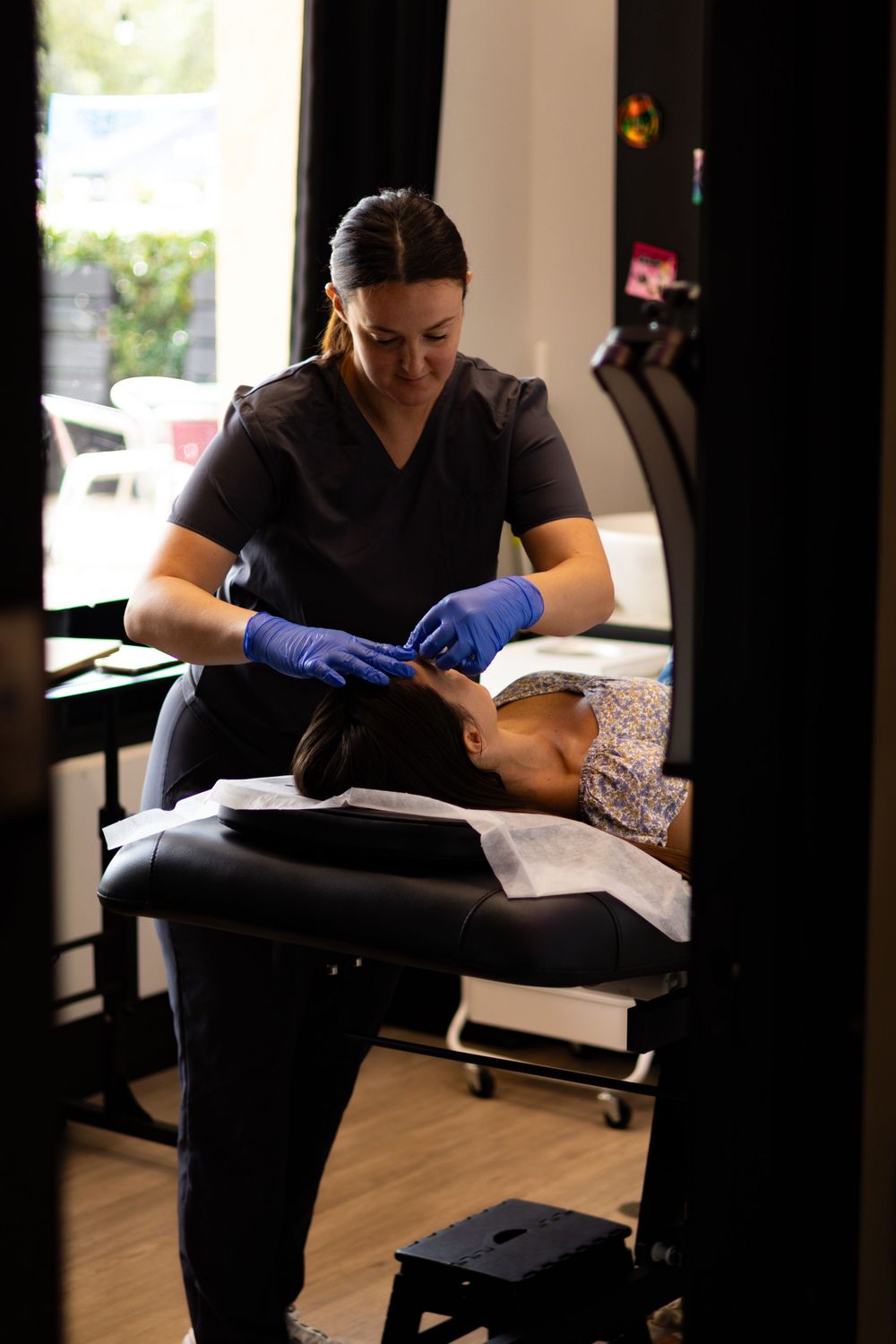 Esthetician in black scrubs performing a skincare treatment in a modern spa setting.