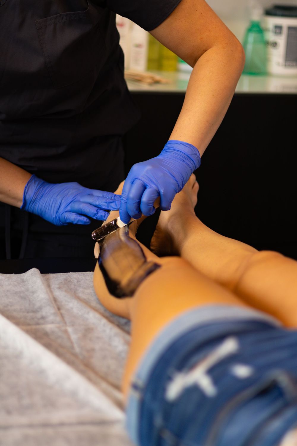 Medical professional in black uniform and blue gloves performing facial procedure.