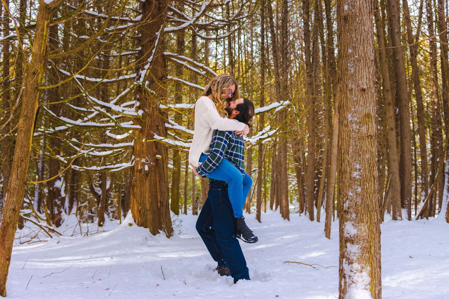 Couple embracing in a snowy winter forest with sunlit trees.