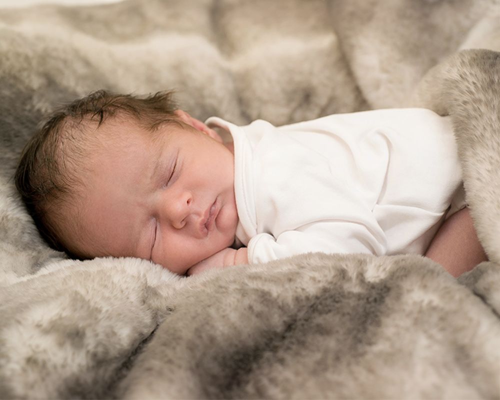 Newborn peacefully sleeping on a soft blanket, dressed in a white outfit, captured by Abigail's Studio in Buckinghamshire.