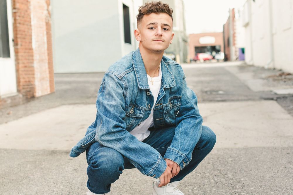 Person in denim jacket posing against urban brick wall backdrop.