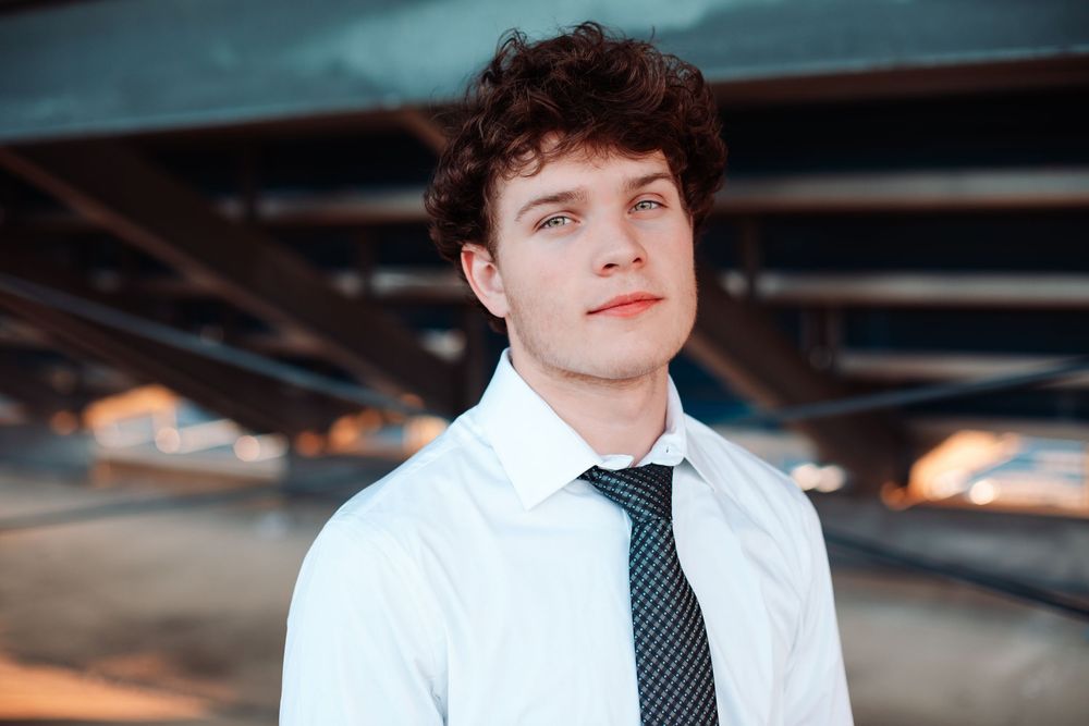 Person in formal attire with tie photographed in dramatic lighting under architectural structure.