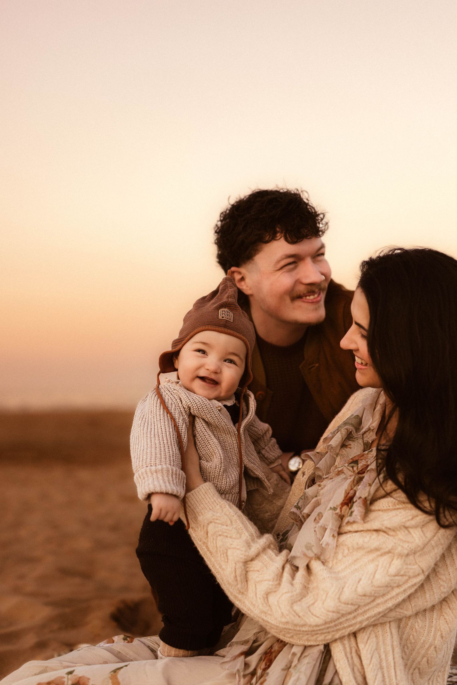 A family shares an intimate moment together in Denia during golden hour sunset, wearing cozy sweaters on a beach. Denia photographer