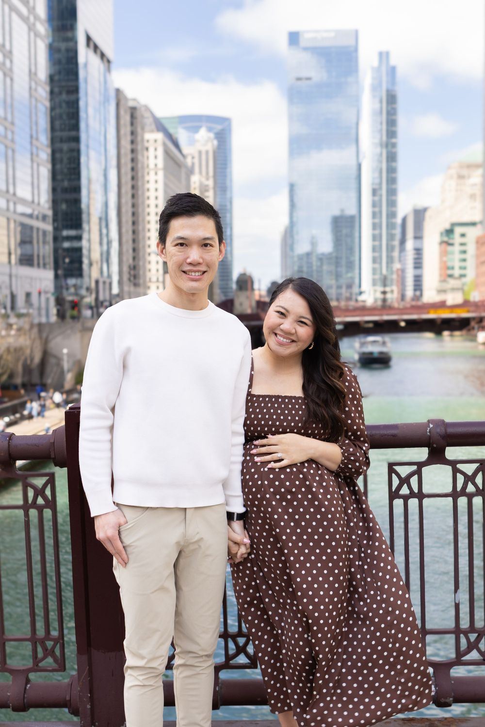 Smiling couple posing on a bridge with Chicago River and city skyline in the background.