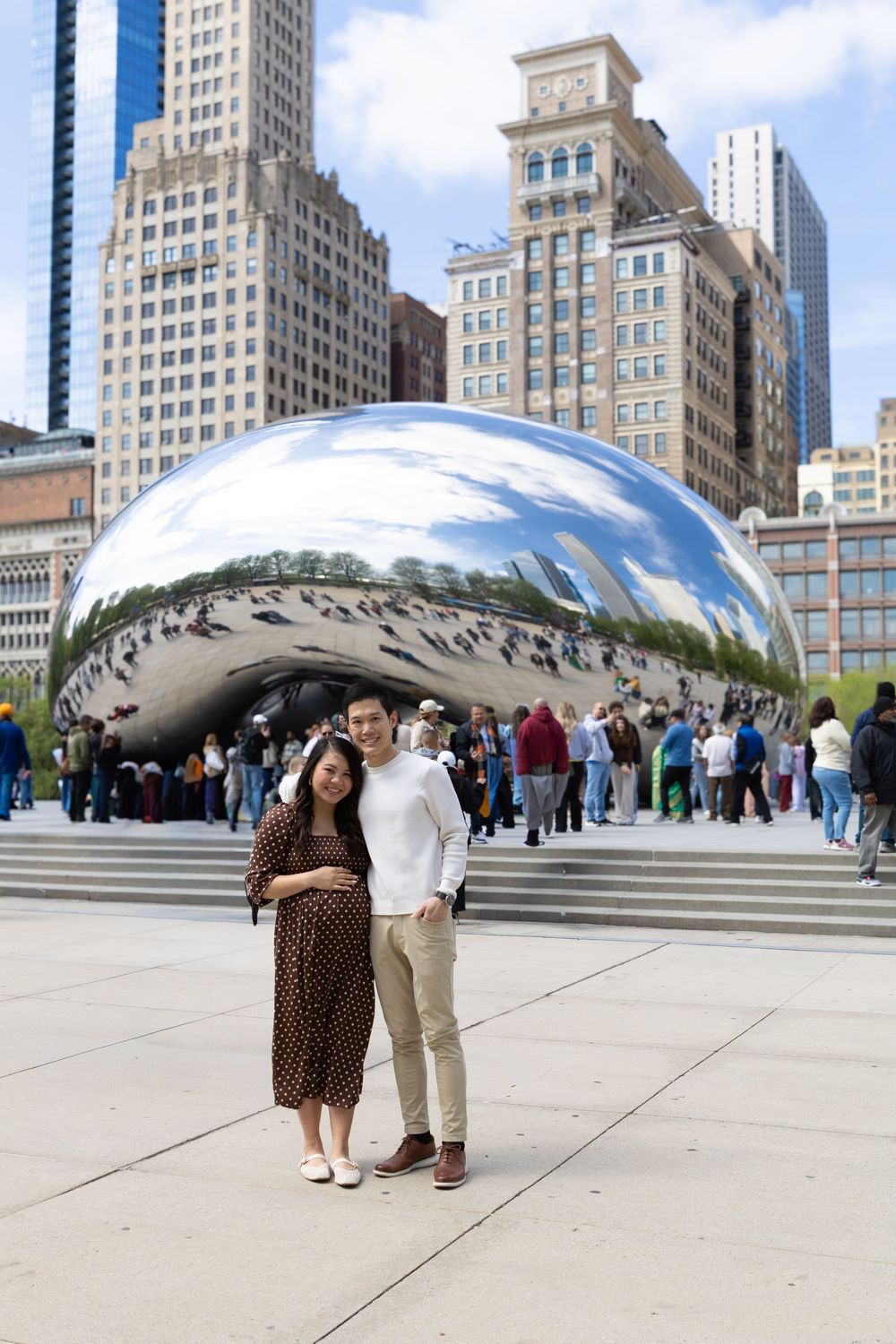 Couple posing in front of Cloud Gate sculpture in Millennium Park, Chicago, with city skyline backdrop.