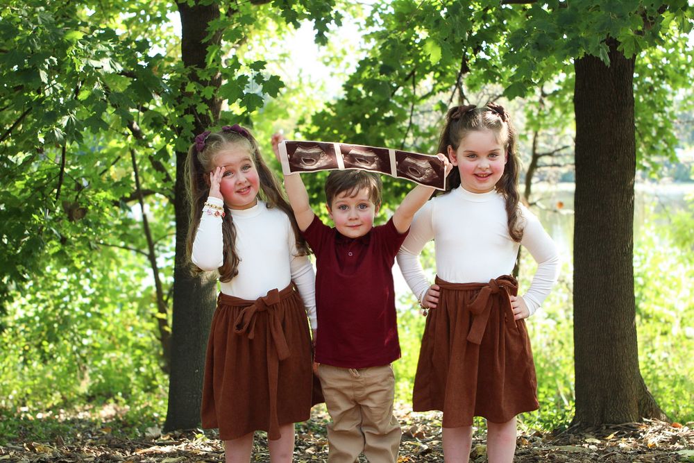 Children in coordinated burgundy and brown outfits play together under trees.