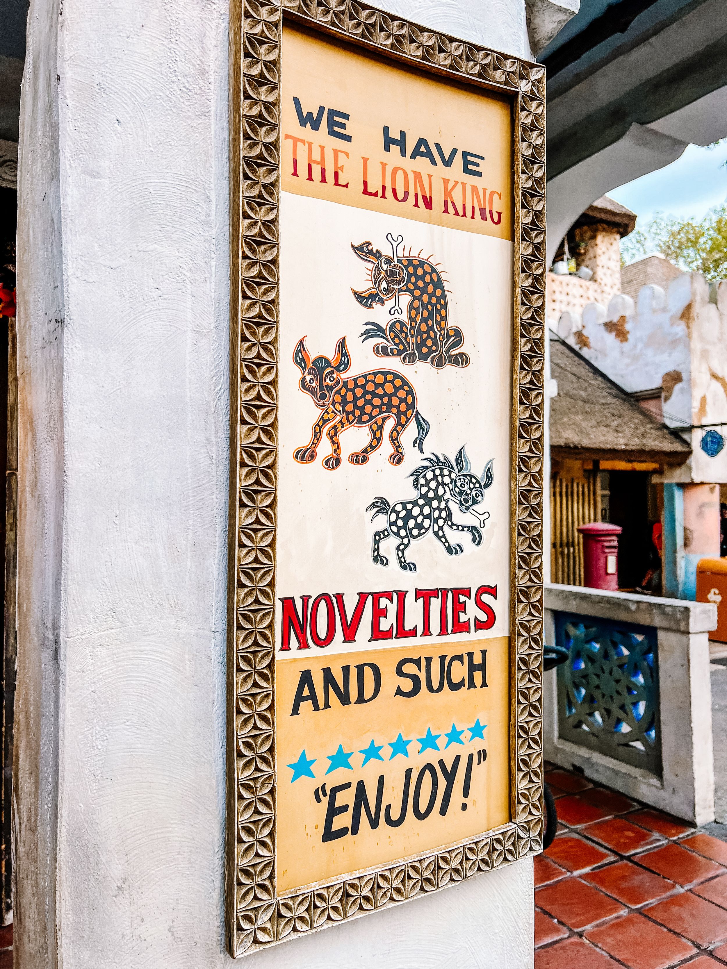 Vintage wall sign displaying 'The Lion King Novelties and Such' with decorative animal silhouettes and ornate border.