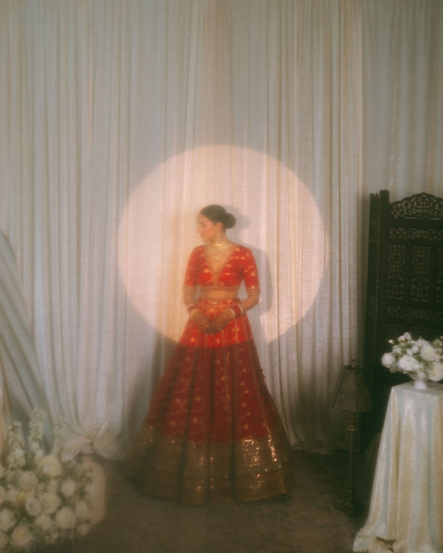 Traditional red and gold Indian bridal lehenga with intricate embroidery displayed against white draped fabric backdrop.