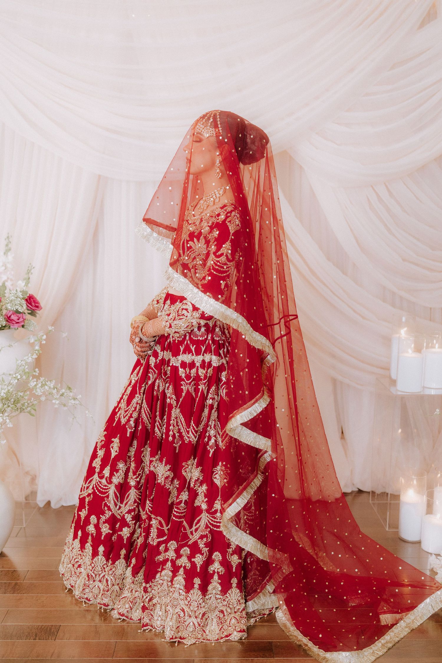 Traditional red and gold Indian bridal lehenga with intricate embroidery displayed against white draped fabric backdrop.