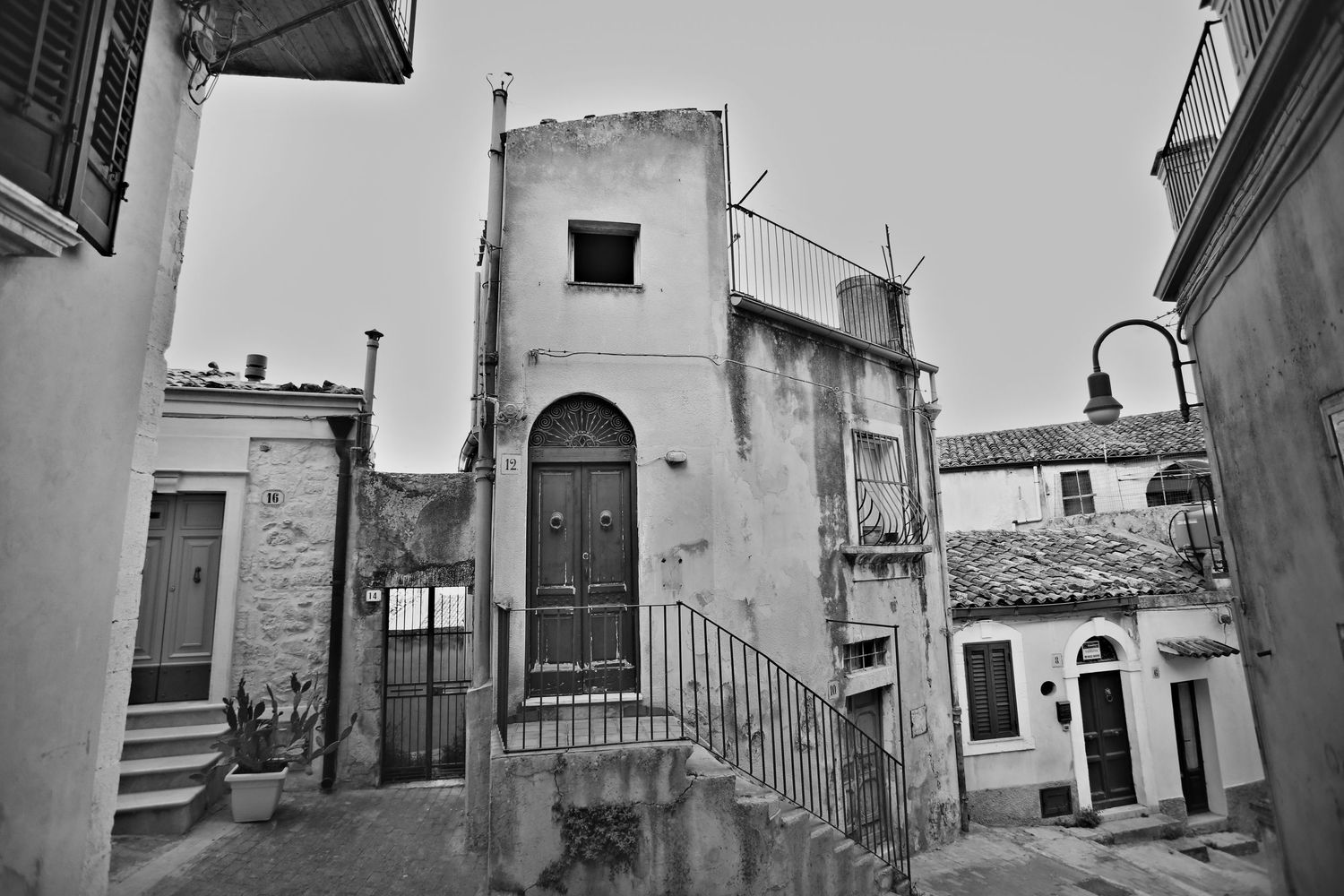 Black and white view of an old rustic Italian building facade with curved stone stairs and arched doorway.