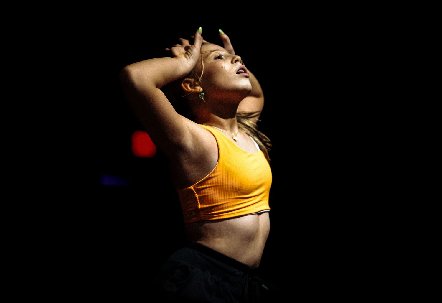 Woman in orange crop top dancing expressively against a dark background with dramatic lighting.