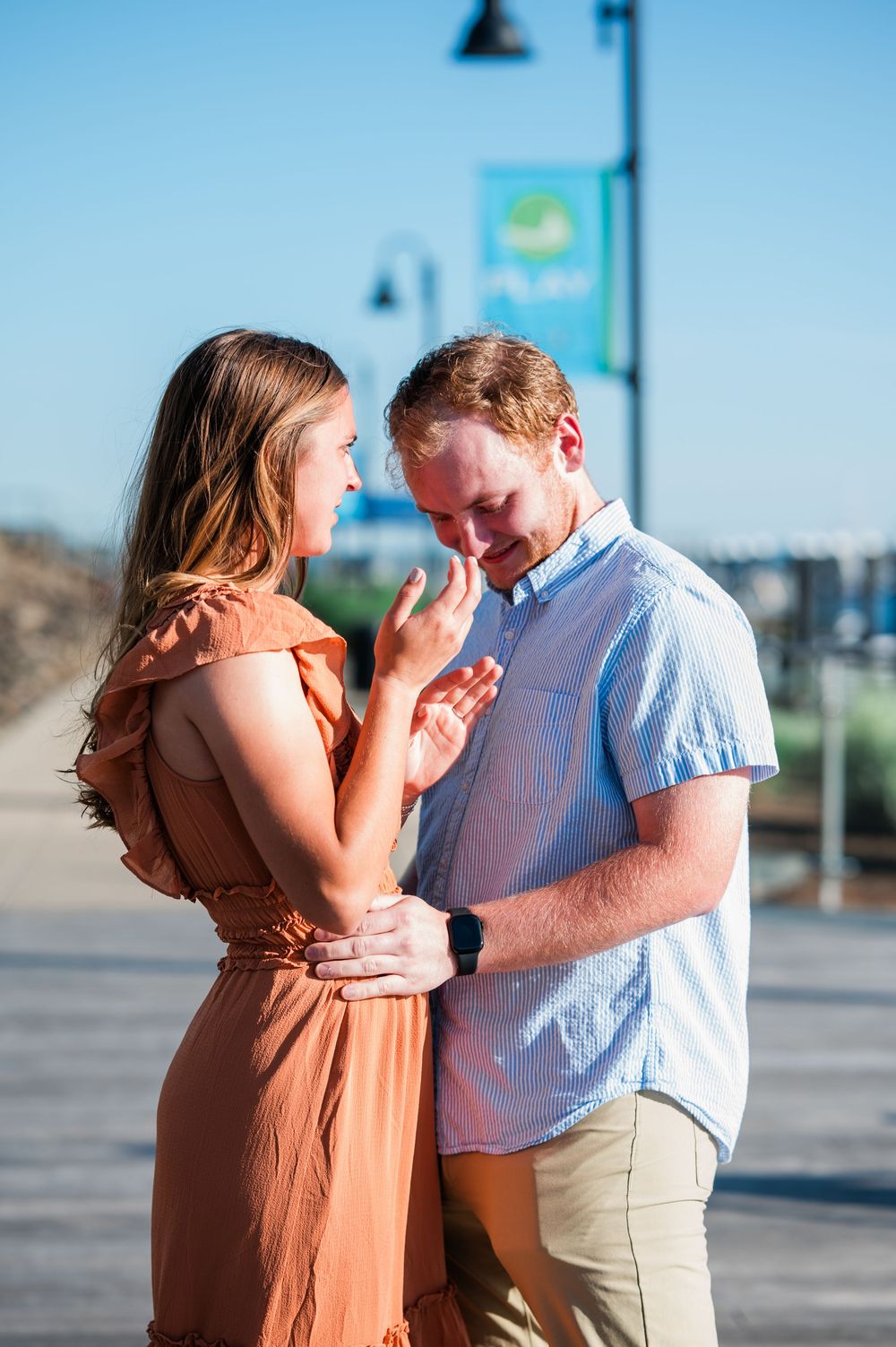 A couple shares romantic moments in a parking lot on a sunny day wearing orange dress and blue shirt. Harbor Point Boardwalk in Stamford, CT