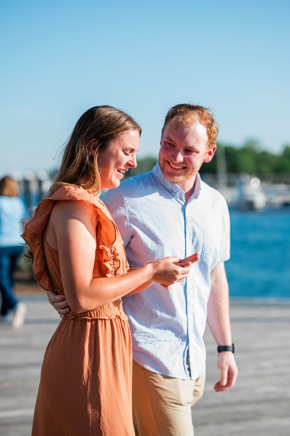 A couple shares a joyful moment together on a waterfront boardwalk on a sunny day. Harbor Point Boardwalk in Stamford, CT