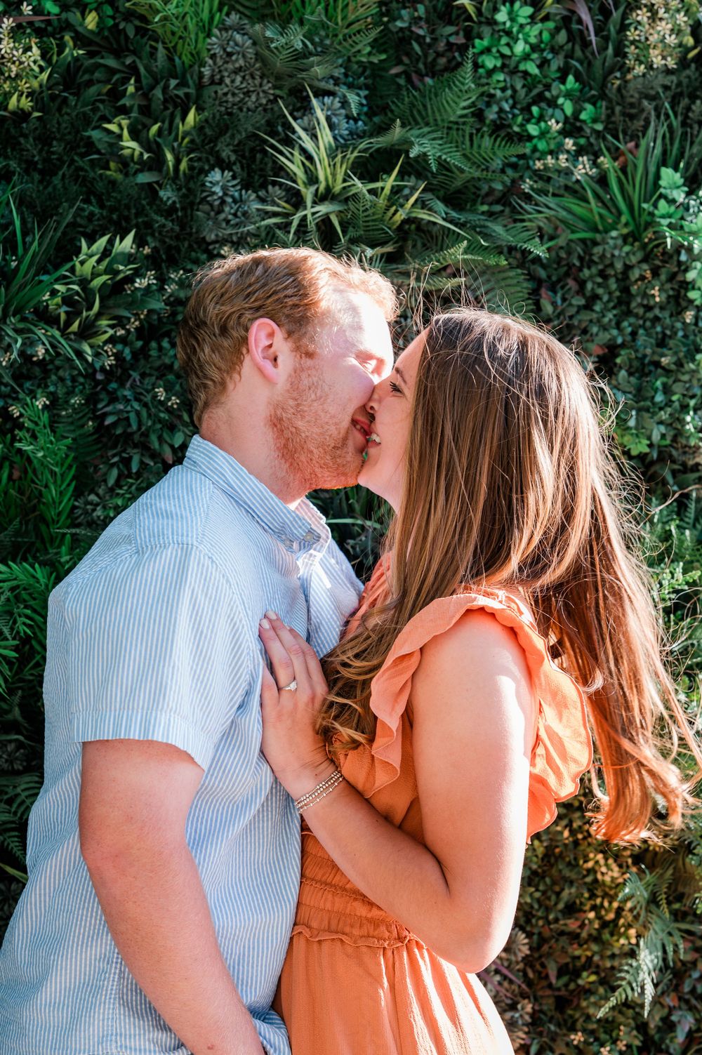 A couple shares an intimate moment outdoors surrounded by lush greenery. Harbor Point Boardwalk in Stamford, CT