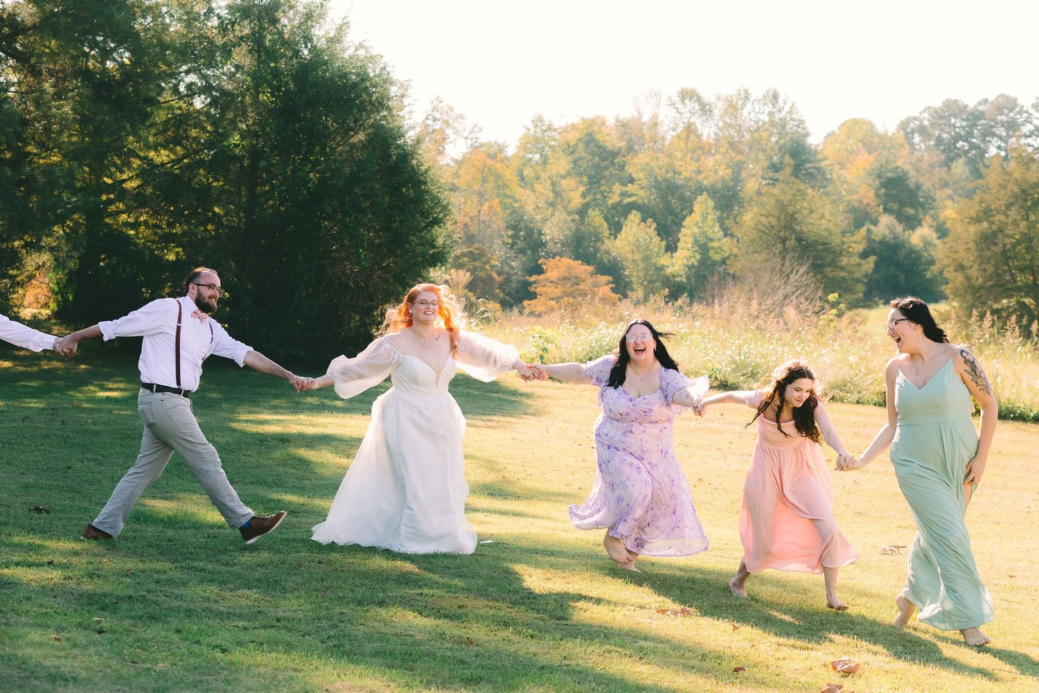 A group dances and celebrates together in a sunlit meadow during golden hour, creating a joyful outdoor scene.