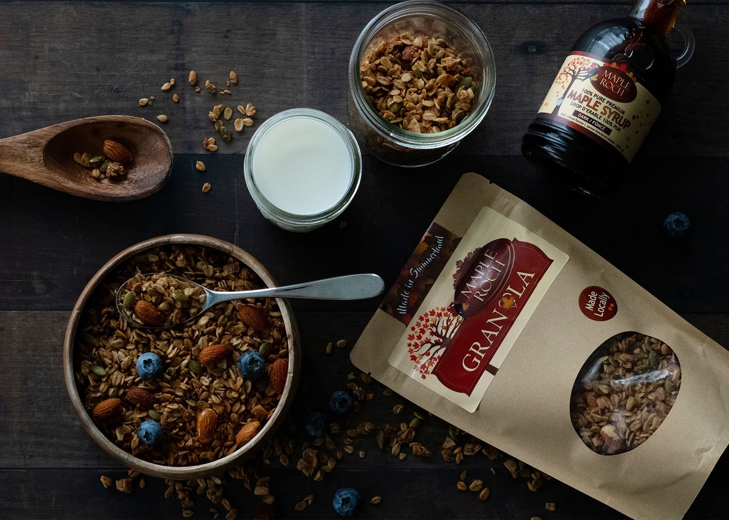 Styled flat lay of artisan granola packaging with bowl, spoon, and fresh ingredients on dark background.