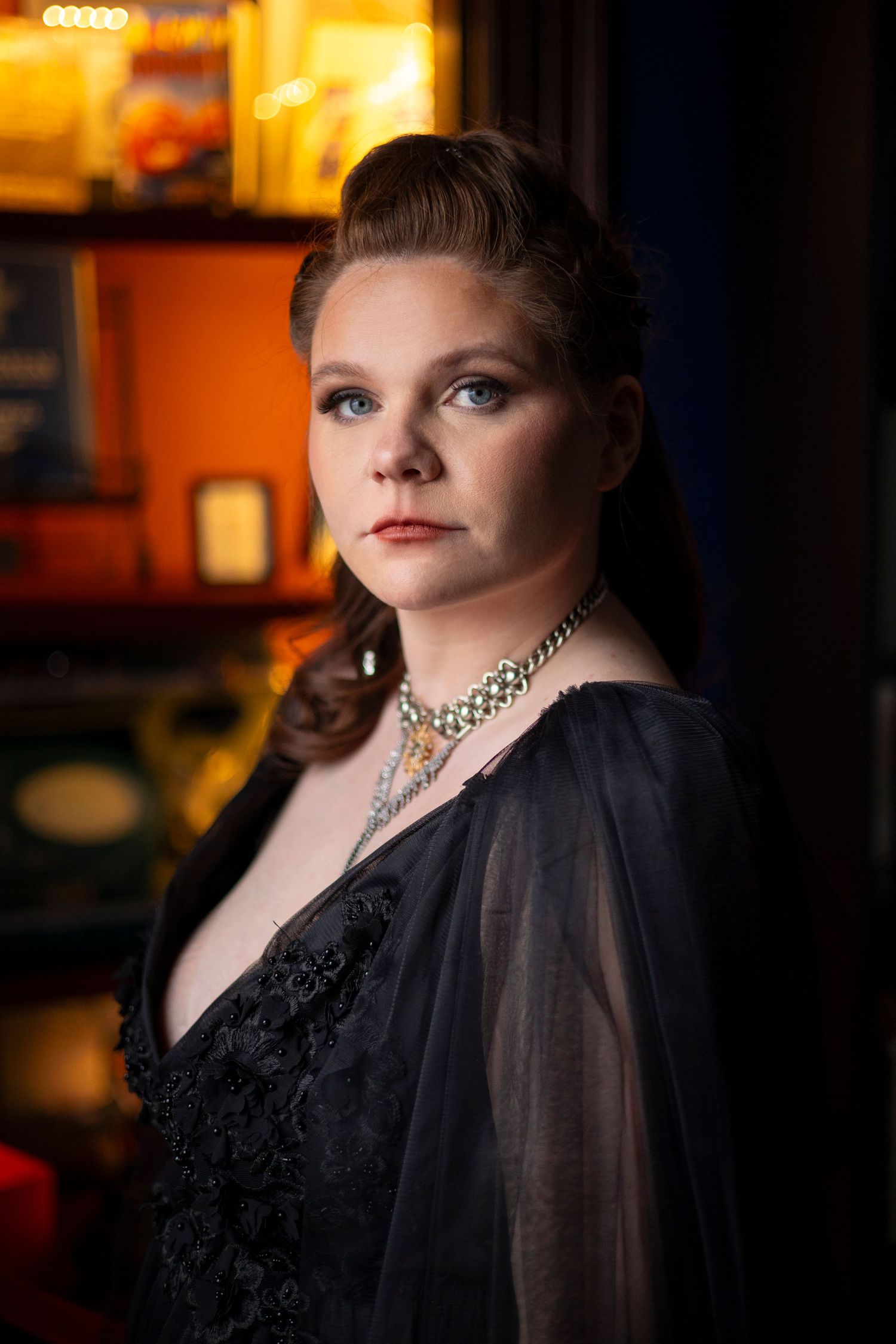 A bride in a black lace dress with sheer sleeves and statement necklace poses for her portrait.