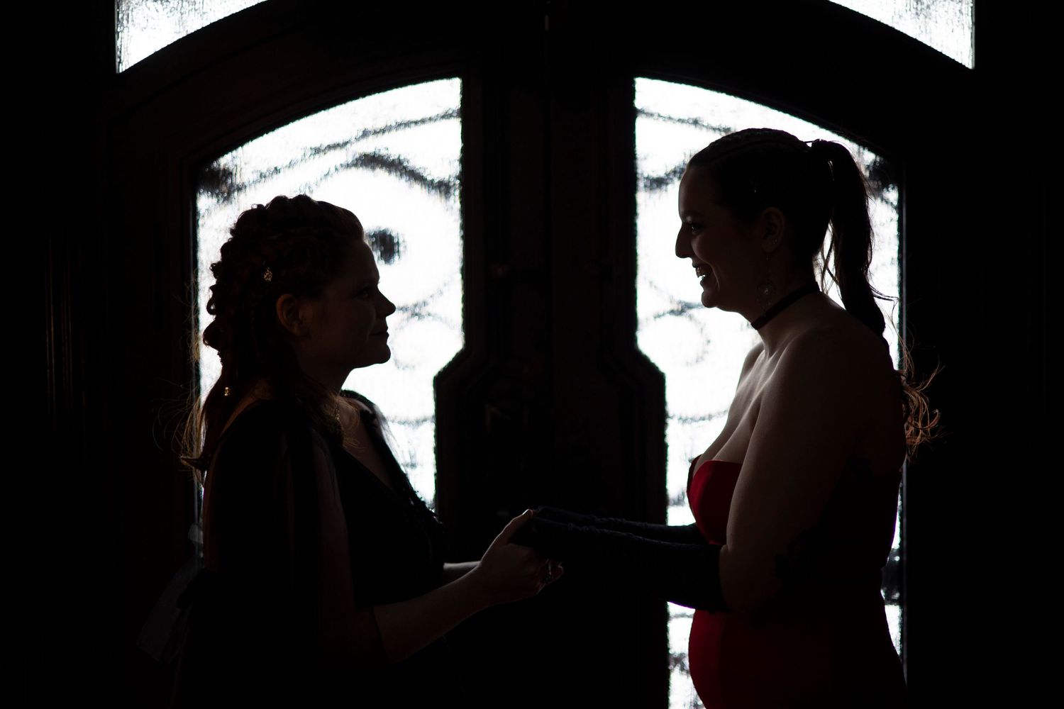 Two engaged women are silhouetted against the front doors of the Satanic Temple.
