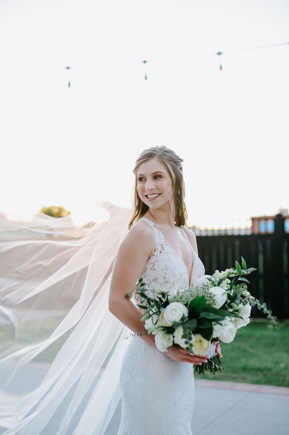 A flowing cathedral veil billows in the wind during an outdoor bridal portrait session.