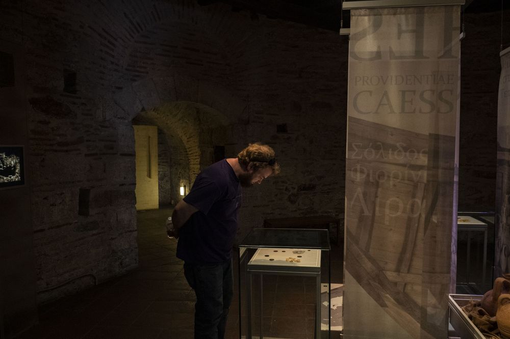 A person leans over to examine a museum display case in a dimly lit exhibition space.