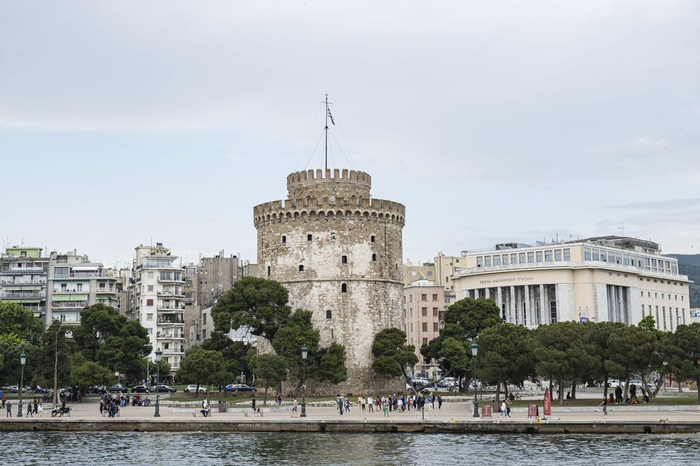 Panoramic view of the White Tower and surrounding buildings in Thessaloniki, Greece with modern architecture visible.