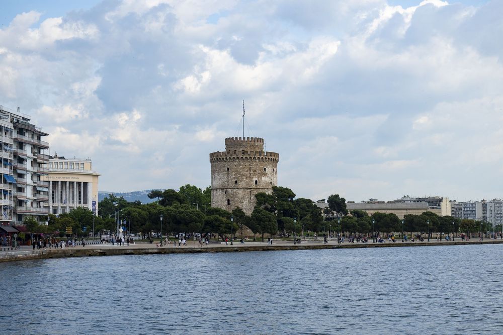 Panoramic view of Thessaloniki's waterfront promenade with the White Tower and modern buildings under cloudy skies.