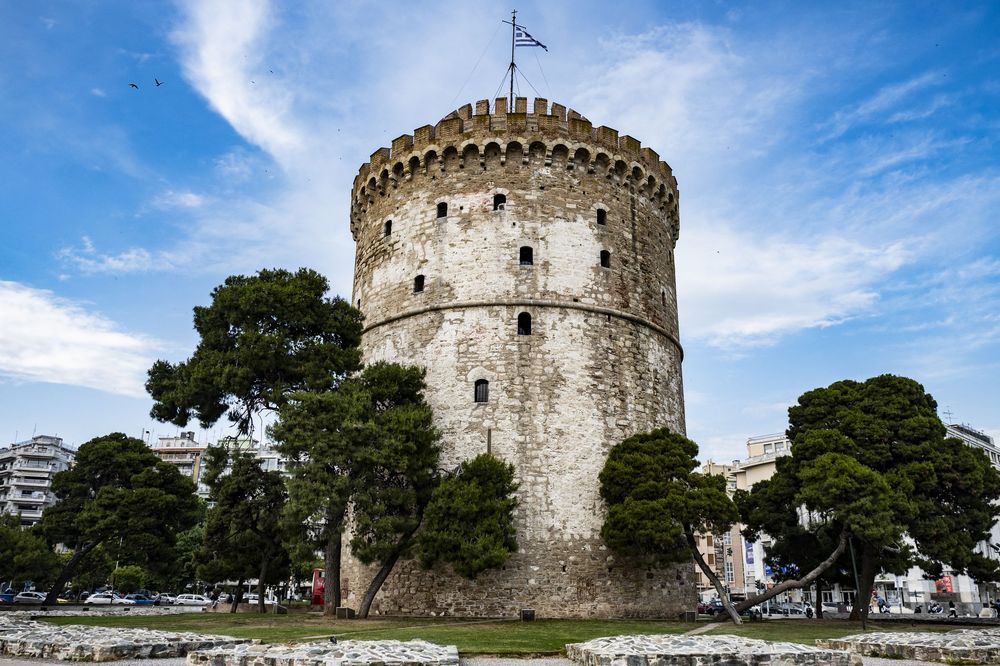 Ancient stone fortress tower with circular architecture stands against bright blue sky in Thessaloniki, Greece.