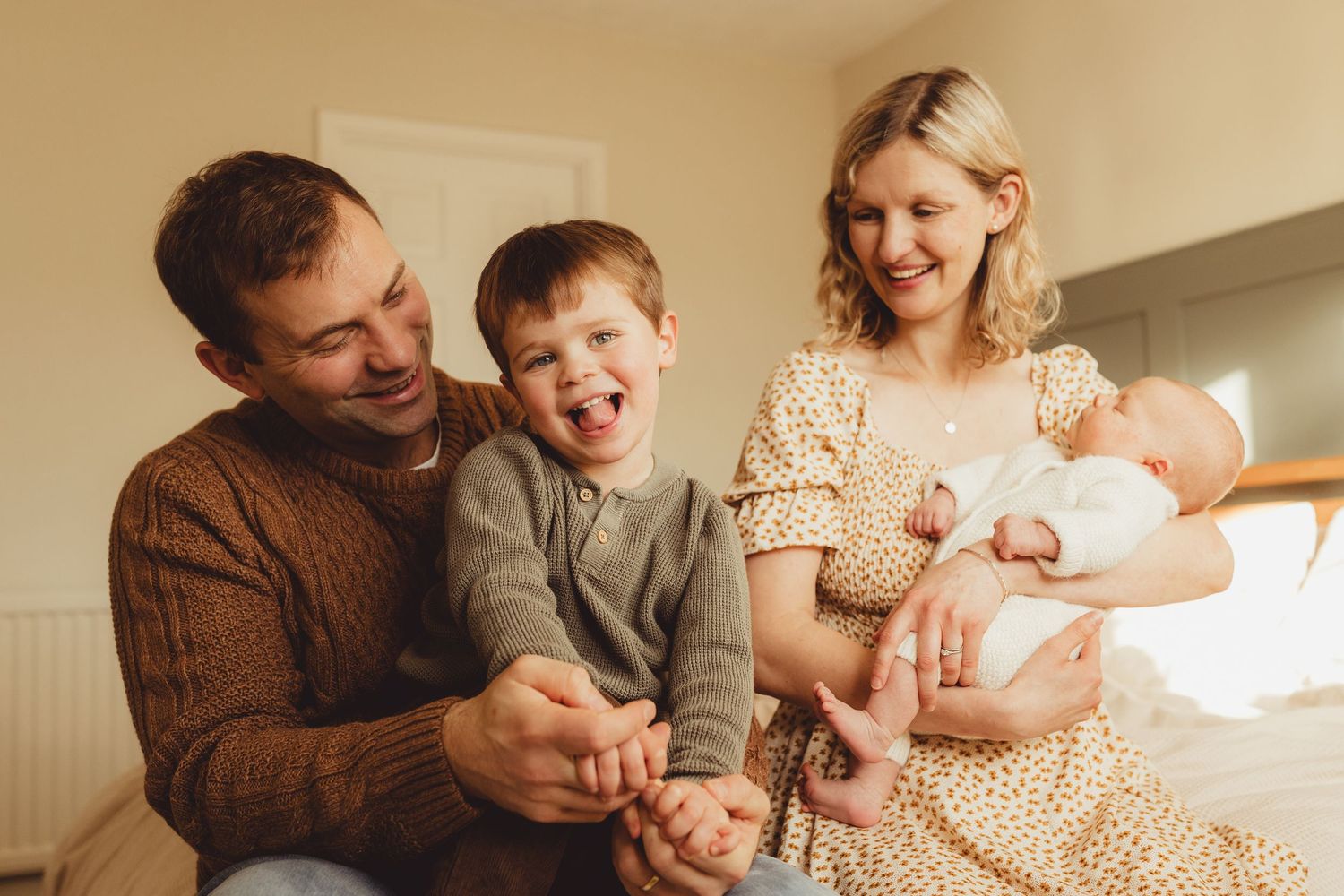 A tender family moment as parents gaze lovingly at their newborn baby near a bright window.