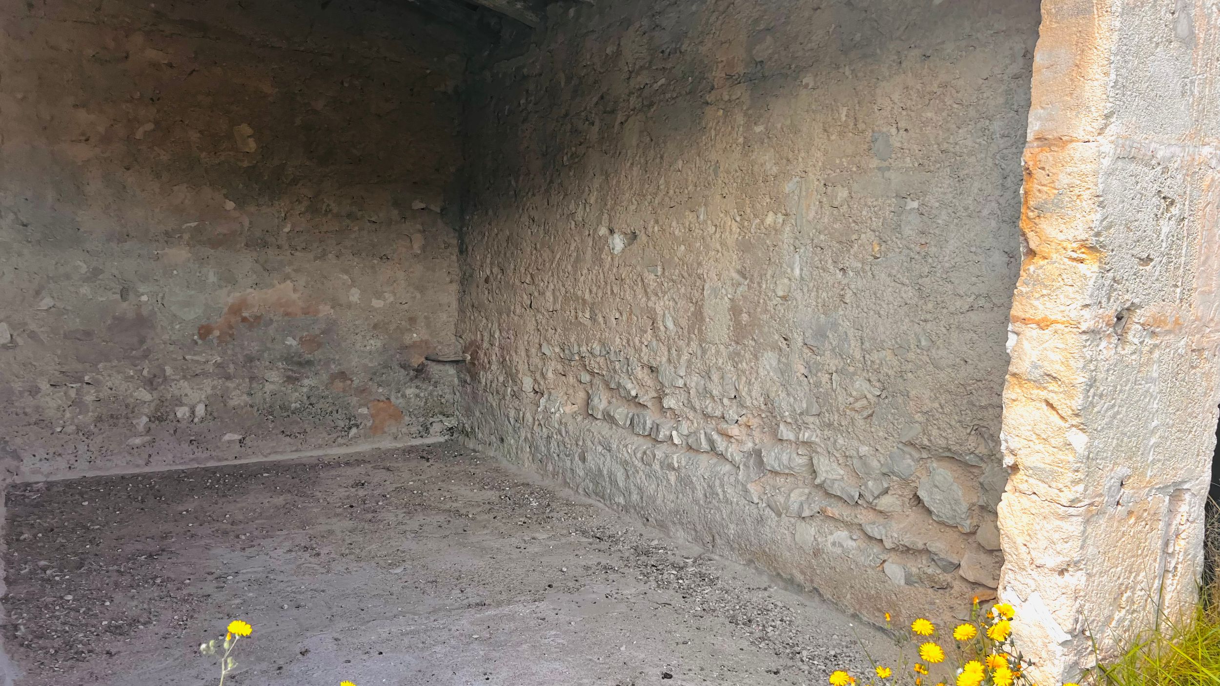 An interior view of a dimly lit, dilapidated room with rough stone walls and a small object on the floor.
