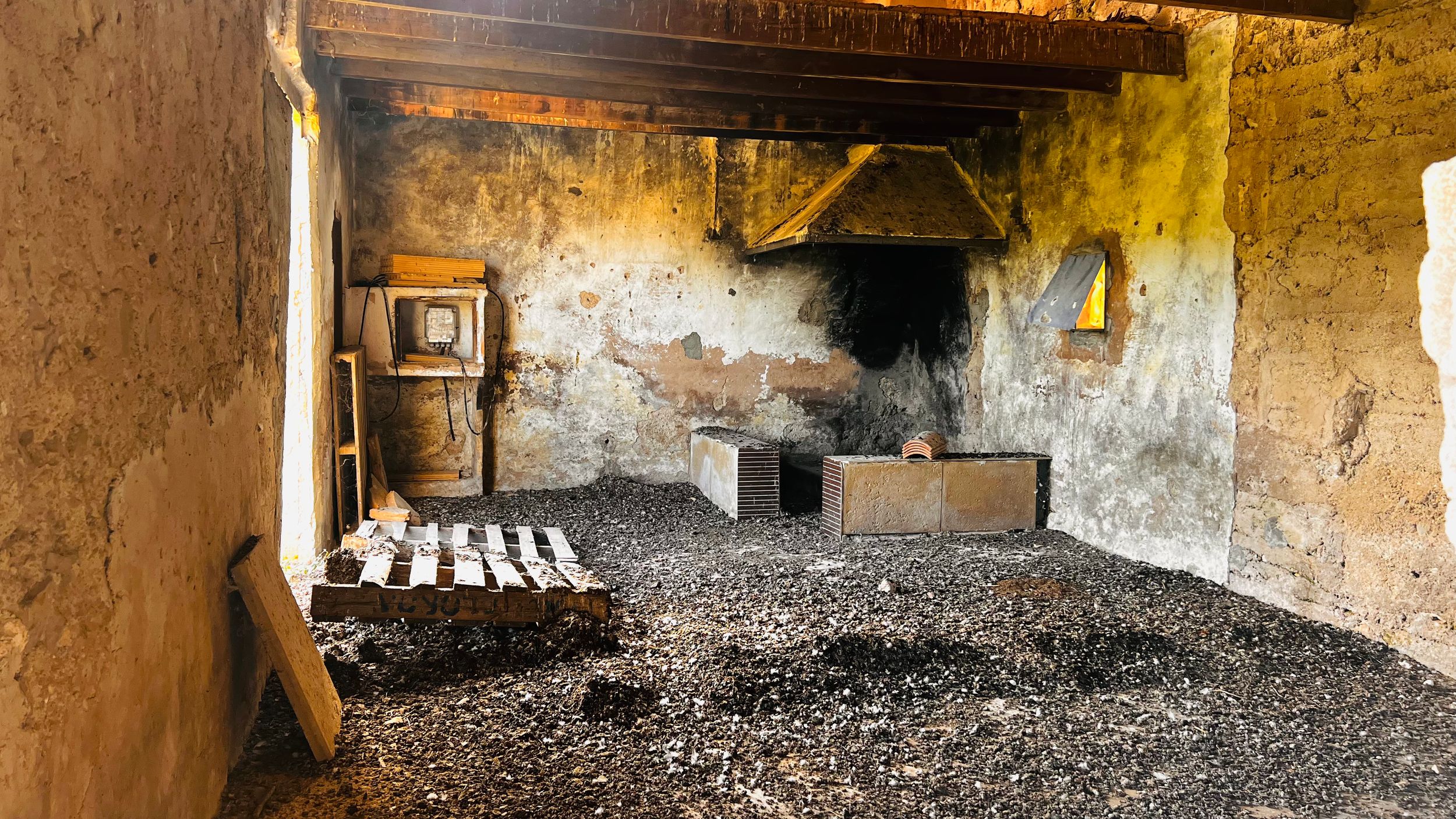An old, dilapidated interior with a wooden ceiling, furniture, and debris on the floor.